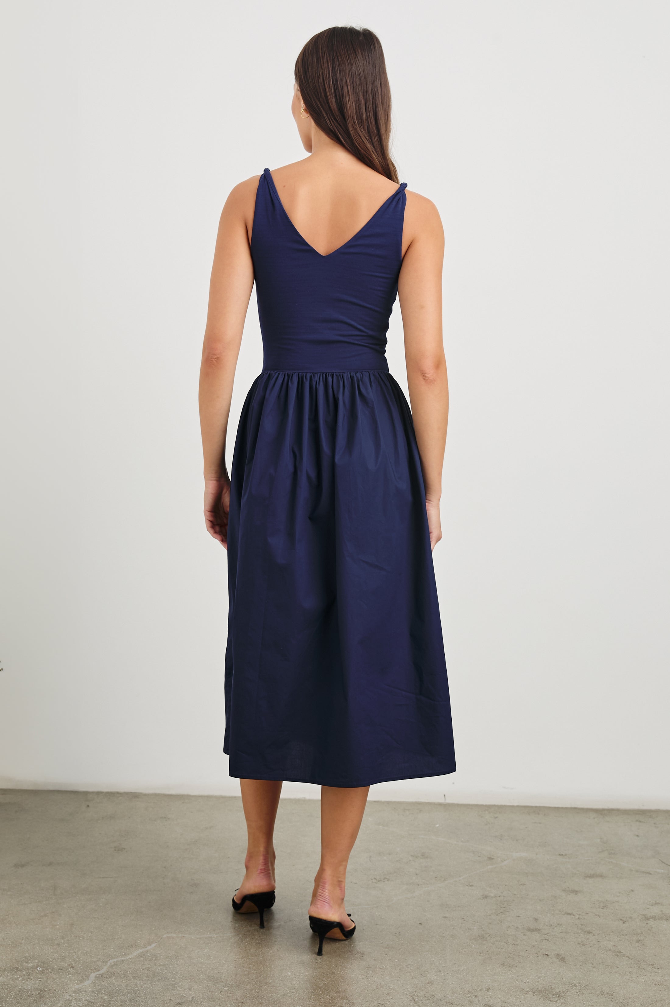 Franca Sleeveless Midi Dress with Twisted Shoulder Straps, a deep V Neck and Pleats at the Waist in Navy Colorway - Back Full Body View Featured on Model
